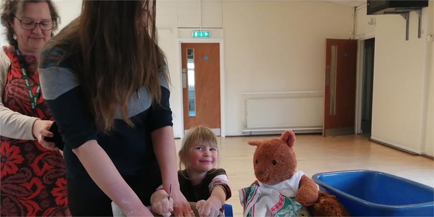 Small child enjoying messy play with adult helpers